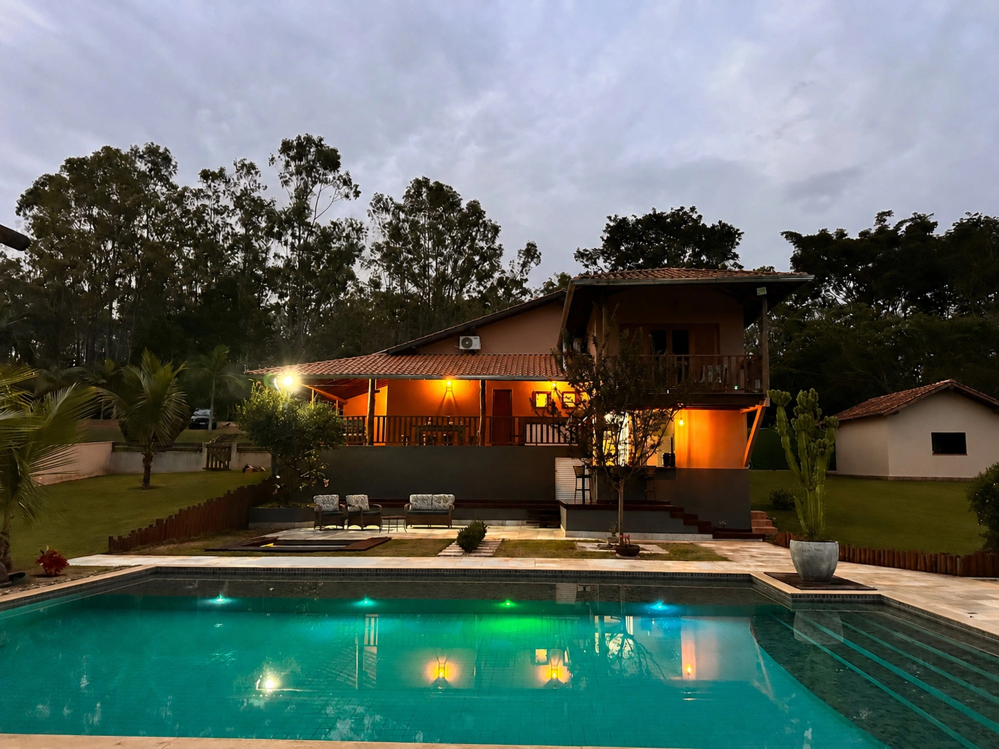 Fachada iluminada da pousada refletida na piscina ao entardecer