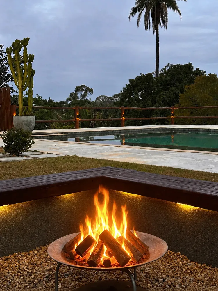 Fogo de chão aceso junto à piscina e à área verde da pousada