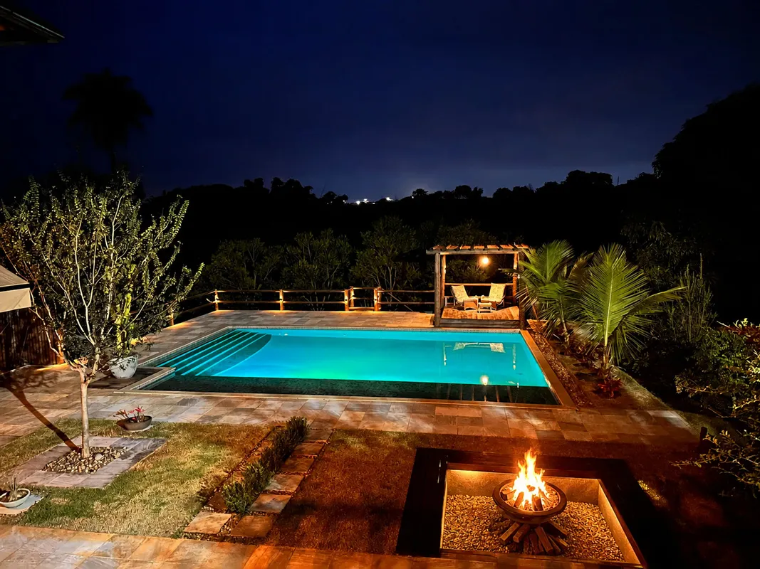 Piscina iluminada e fogo de chão na área externa da pousada à noite