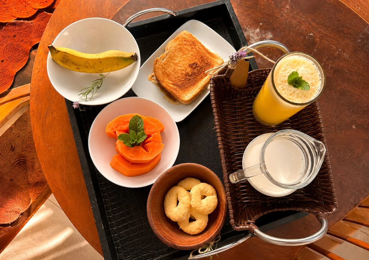 Bandeja de café da manhã com banana, misto quente, mamão, suco e biscoitos
